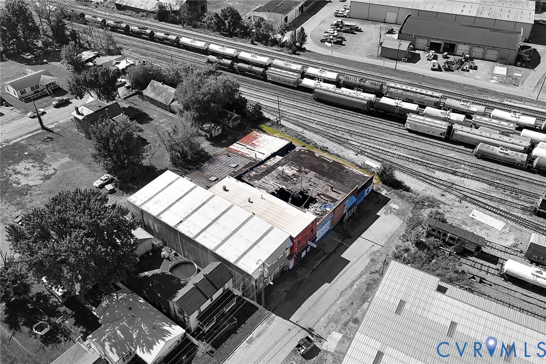 Aerial perspective of a multi-section commercial structure featuring a combination of metal and flat roofing, brick exterior walls, and immediate proximity to rail infrastructure