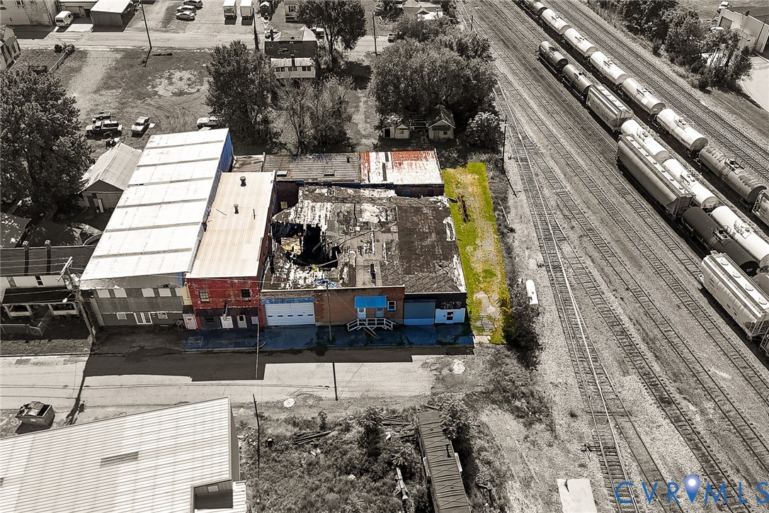 Aerial perspective of a multi-section commercial structure featuring a combination of brick and metal siding exterior finishes, multiple street-level access points, and a dedicated strip of exterior land Aerial perspective of a multi-section commercial structure featuring a combination of brick and metal siding exterior finishes, multiple street-level access points, and a dedicated strip of exterior land