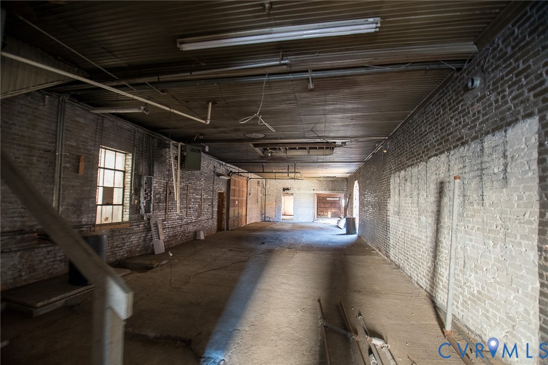 Expansive interior space featuring exposed brick masonry walls, wood-plank ceiling, industrial-style multi-pane windows, and concrete flooring