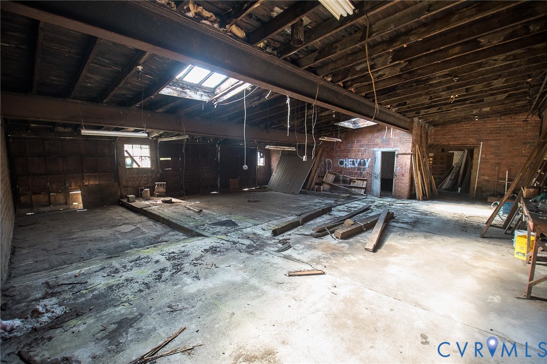 Open-concept interior featuring exposed brick walls, steel support beams, concrete flooring, and multiple ceiling skylights