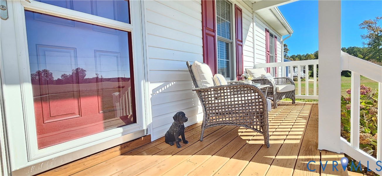 Covered front porch featuring natural wood decking, white vinyl siding, red window shutters, and white railings