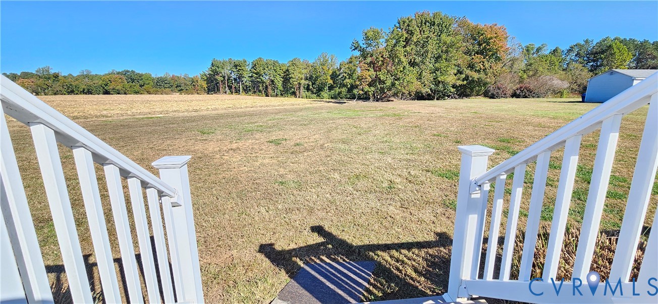 Expansive lot featuring white vinyl railings, open acreage, and mature tree line