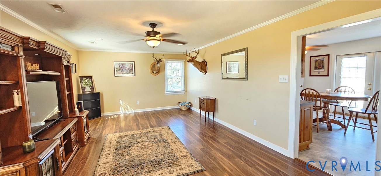 Living area featuring wood-finish flooring, a ceiling fan with integrated light fixture, and a built-in wooden media center