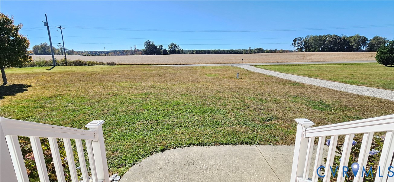 White vinyl staircase railing overlooking an expansive lawn, concrete walkway, and open agricultural land