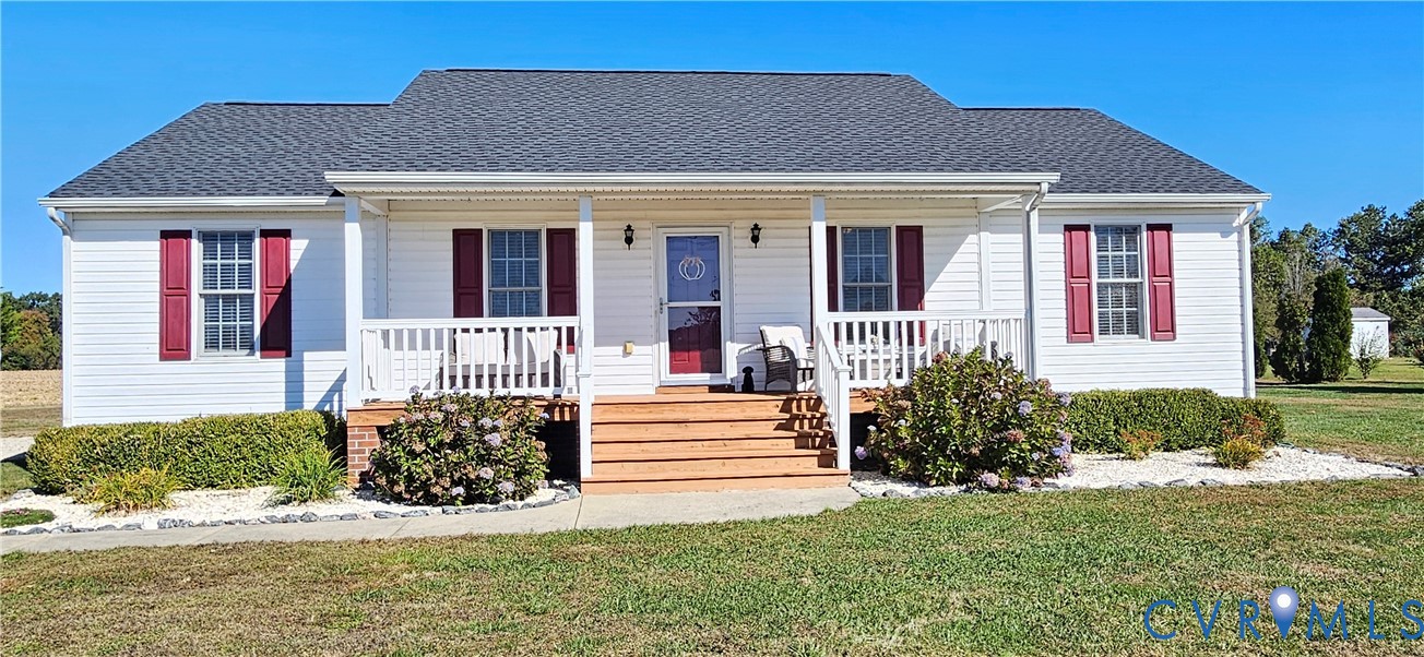 Single-story residence featuring white horizontal siding, a covered front porch with wood-finish decking, dark red louvered shutters, and a shingled roof Single-story residence featuring white horizontal siding, a covered front porch with wood-finish decking, dark red louvered shutters, and a shingled roof