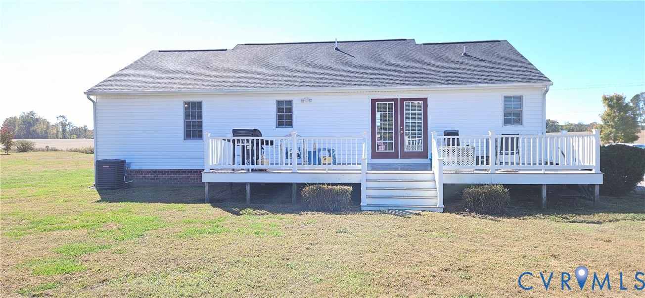 Rear exterior featuring white vinyl siding, a raised white deck with stairs, double glass-panel doors, and brick foundation detailing