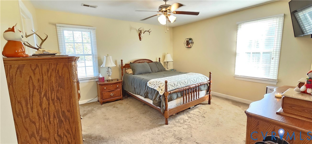Neutral-toned room featuring neutral carpeting, multi-pane windows with integrated blinds, and a ceiling-mounted fan with light fixture