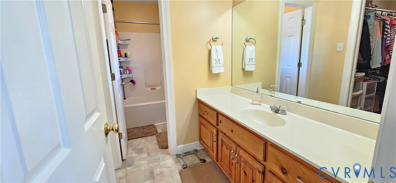 Bathroom featuring a vanity with wood cabinetry, a solid-surface countertop with an integrated sink, a large wall-mounted mirror, and a tub-shower combination with a surround