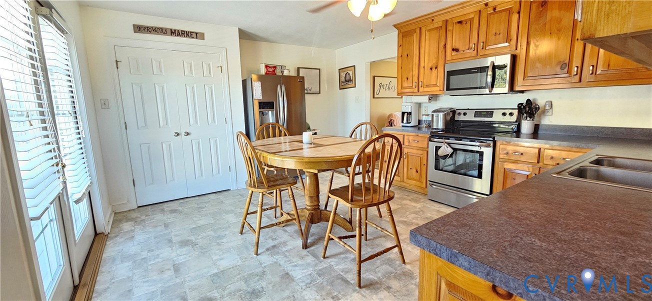 Kitchen featuring natural wood cabinetry, stainless steel appliances, solid-surface countertops, dual-basin stainless steel sink, and glass-paneled double doors