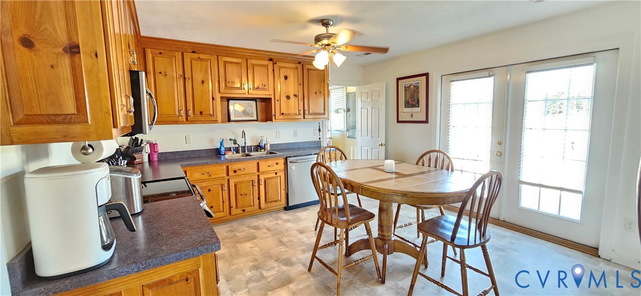 Kitchen featuring knotty wood cabinetry, dark laminate countertops, stainless steel dual-basin sink, integrated ceiling fan, and paneled glass exterior doors