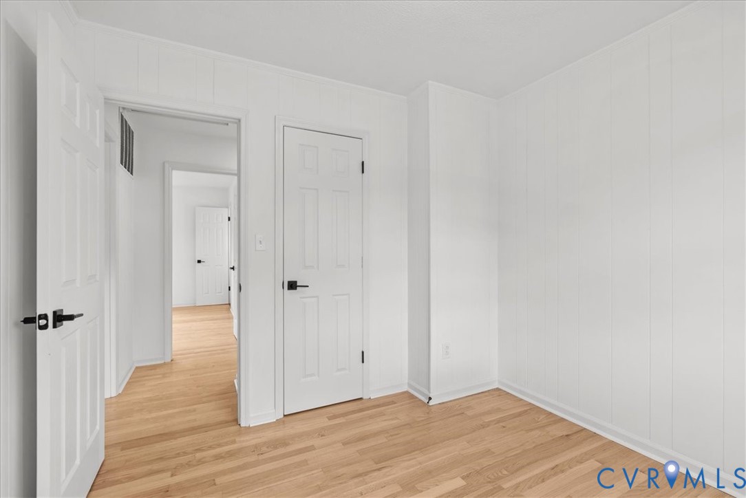Interior space featuring white vertical paneling, wood-finish flooring, and six-panel interior doors with matte black hardware