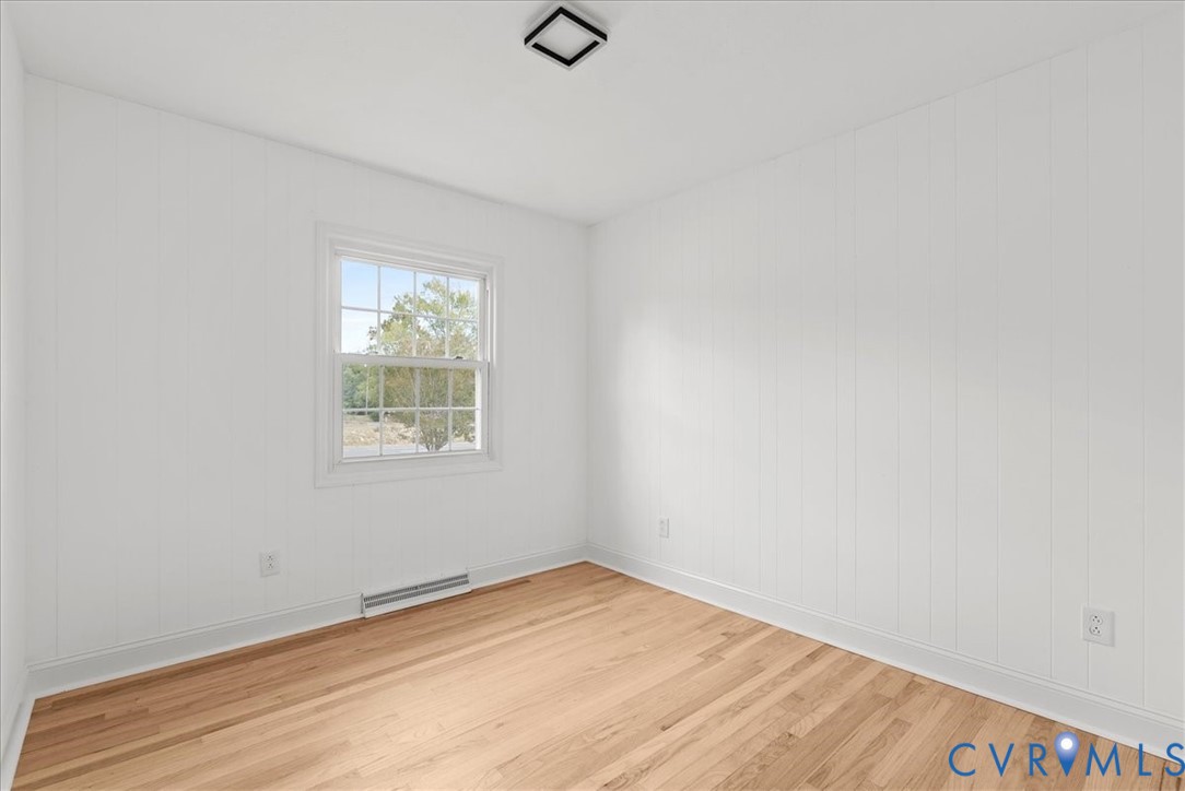 Interior space featuring white vertical paneled walls, wood-finish flooring, a multi-pane window, and a square flush-mount ceiling light