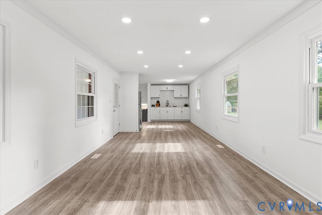 Open interior featuring wood-finish flooring, recessed lighting, white cabinetry, a tiled backsplash, and dual-pane windows