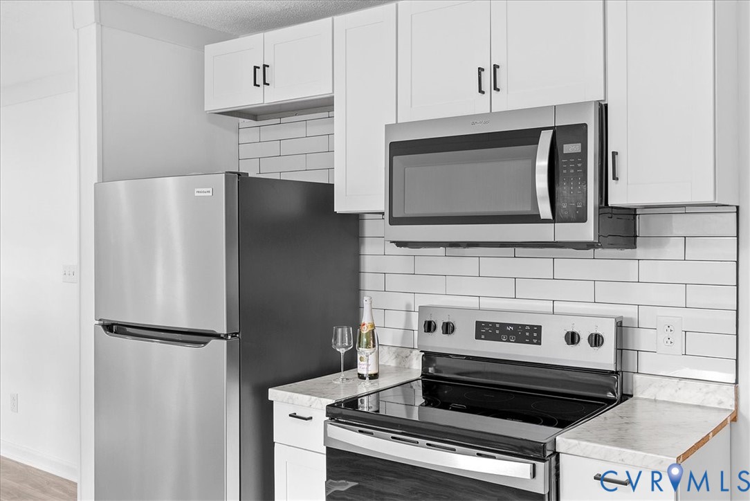 Kitchen featuring white shaker-style cabinetry, stainless steel appliances, subway tile backsplash, and stone-patterned countertops