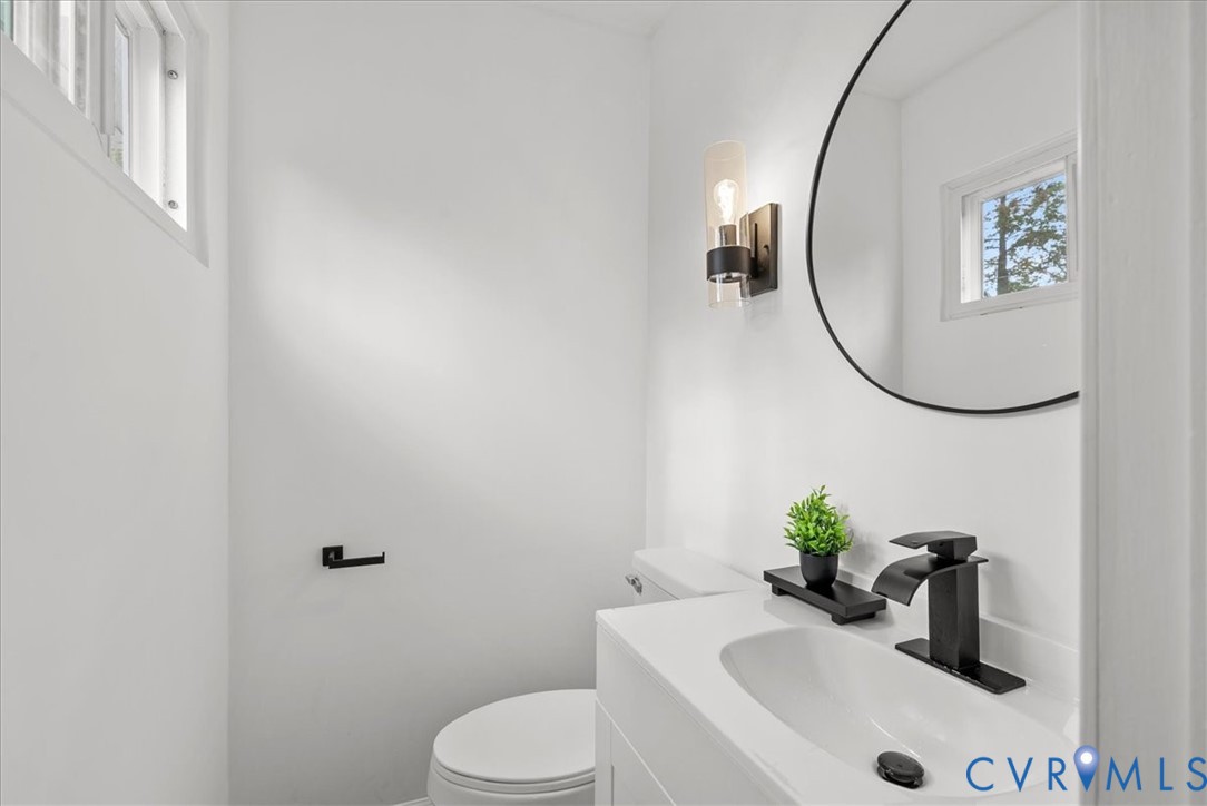 White vanity with a solid surface countertop, undermount sink, matte black widespread faucet, oval mirror, and a wall-mounted cylinder light fixture