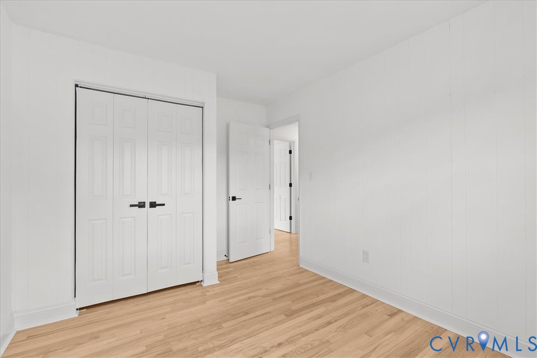 Room featuring white vertical-panel walls, wood-finish flooring, and white interior doors with matte black hardware