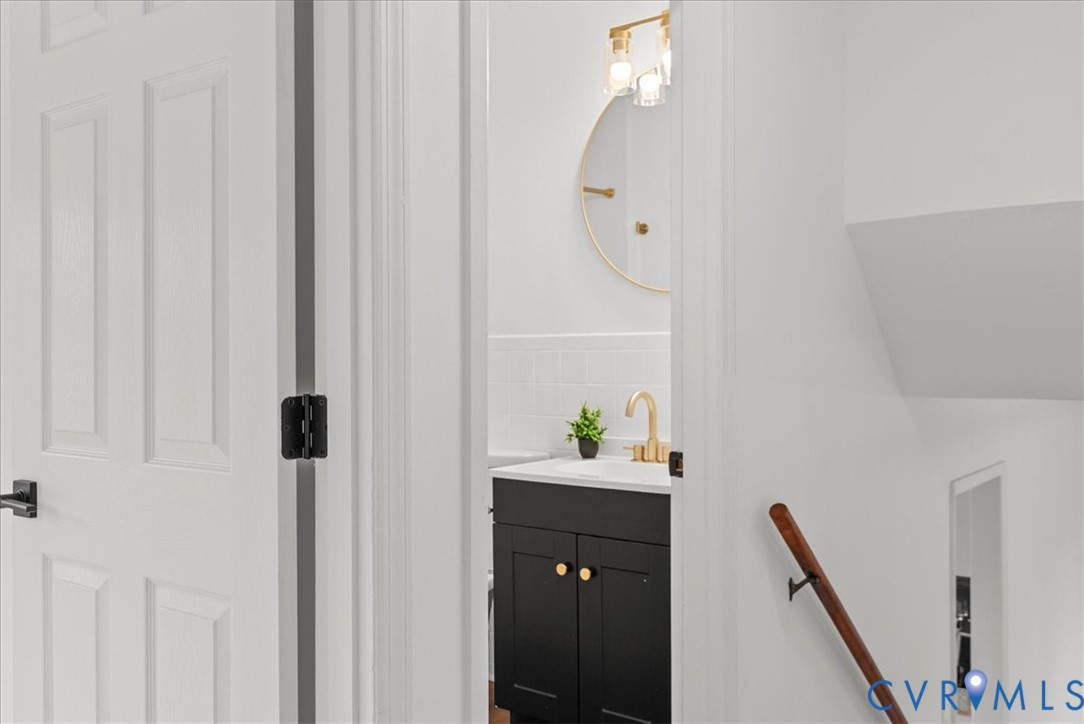 Bathroom featuring a black vanity with a white countertop, gold-tone fixtures, a circular gold-rimmed mirror, and a wall-mounted wood handrail