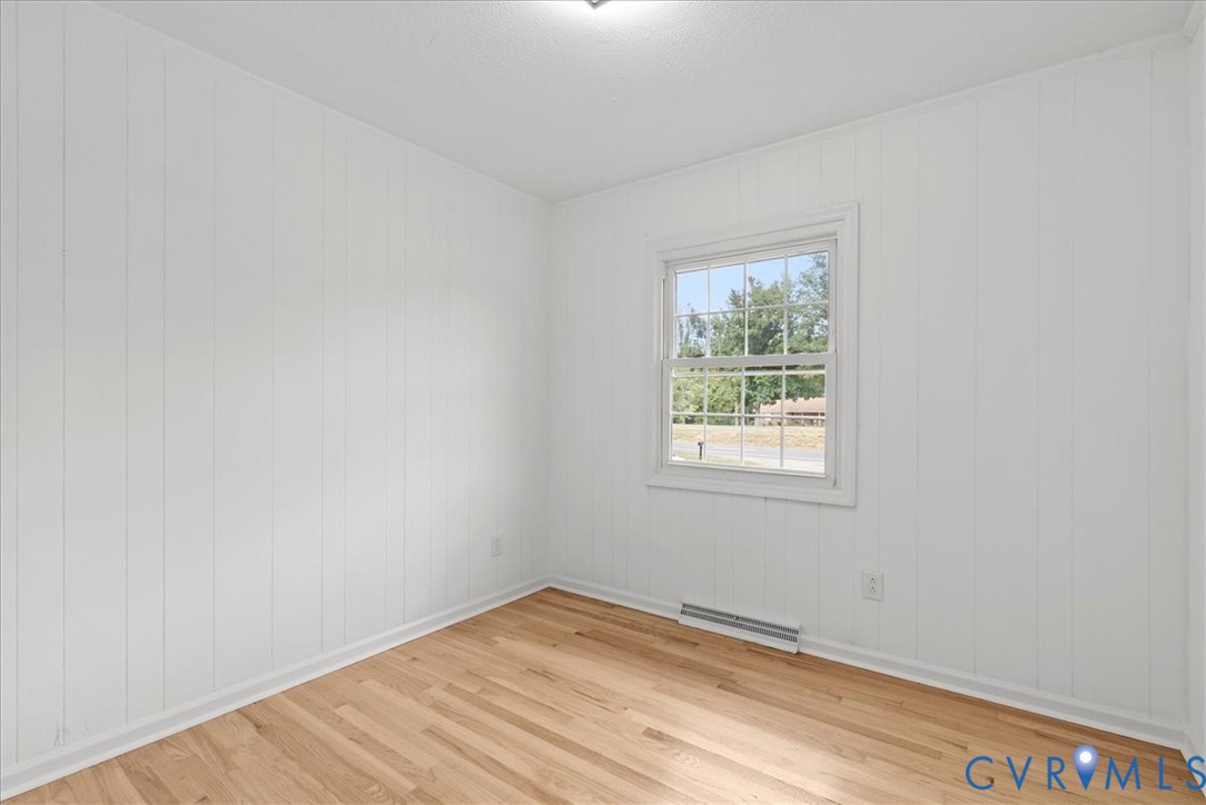 Interior room featuring vertical wood paneling, wood-finish flooring, and a single-hung window with muntin detailing