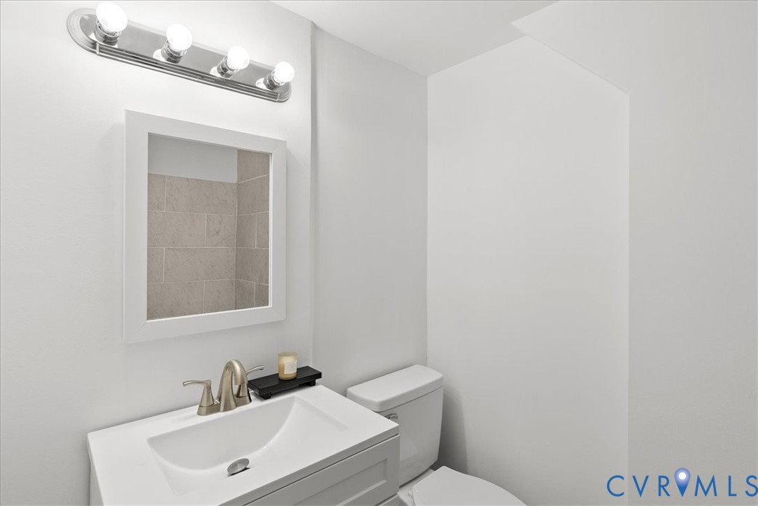 Wall-mounted four-bulb chrome light fixture, square-framed wall mirror, integrated rectangular sink with a brushed-nickel faucet, and a standard-height toilet