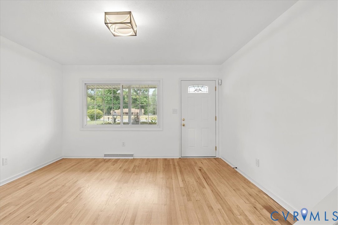 Room featuring wood-finish flooring, a rectangular sliding window, a single-entry door with a decorative glass insert, and a flush-mount rectangular light fixture