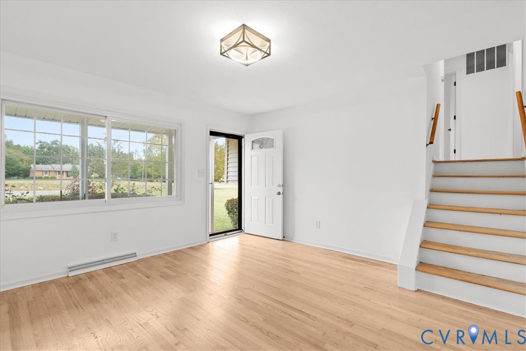 Interior space featuring wood-finish flooring, a large picture window, a geometric ceiling-mounted light fixture, and a wooden staircase with white risers