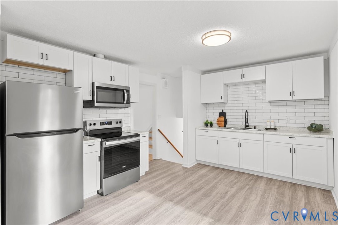 Kitchen featuring white cabinetry, stainless steel appliances, subway tile backsplash, stone-finish countertops, and wood-finish flooring