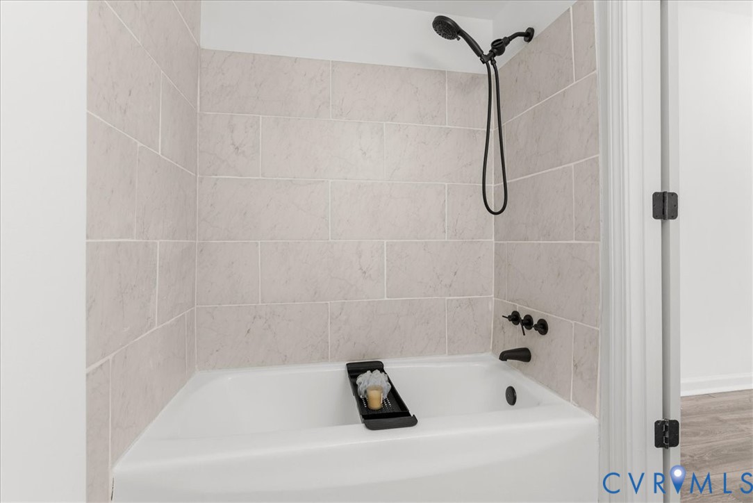 Bathtub surround featuring light-toned, large-format subway tiles, matte black wall-mounted fixtures, and a handheld showerhead