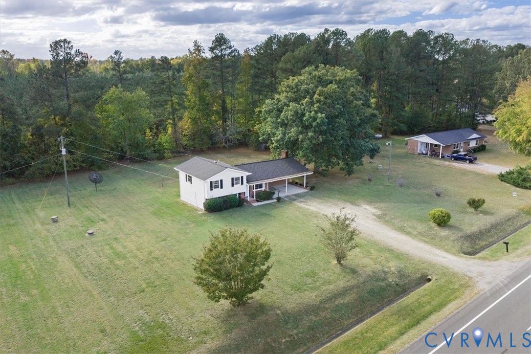 Single-story residence featuring a covered carport, light-colored siding, dark shingled roof, expansive lot, and mature tree-lined perimeter