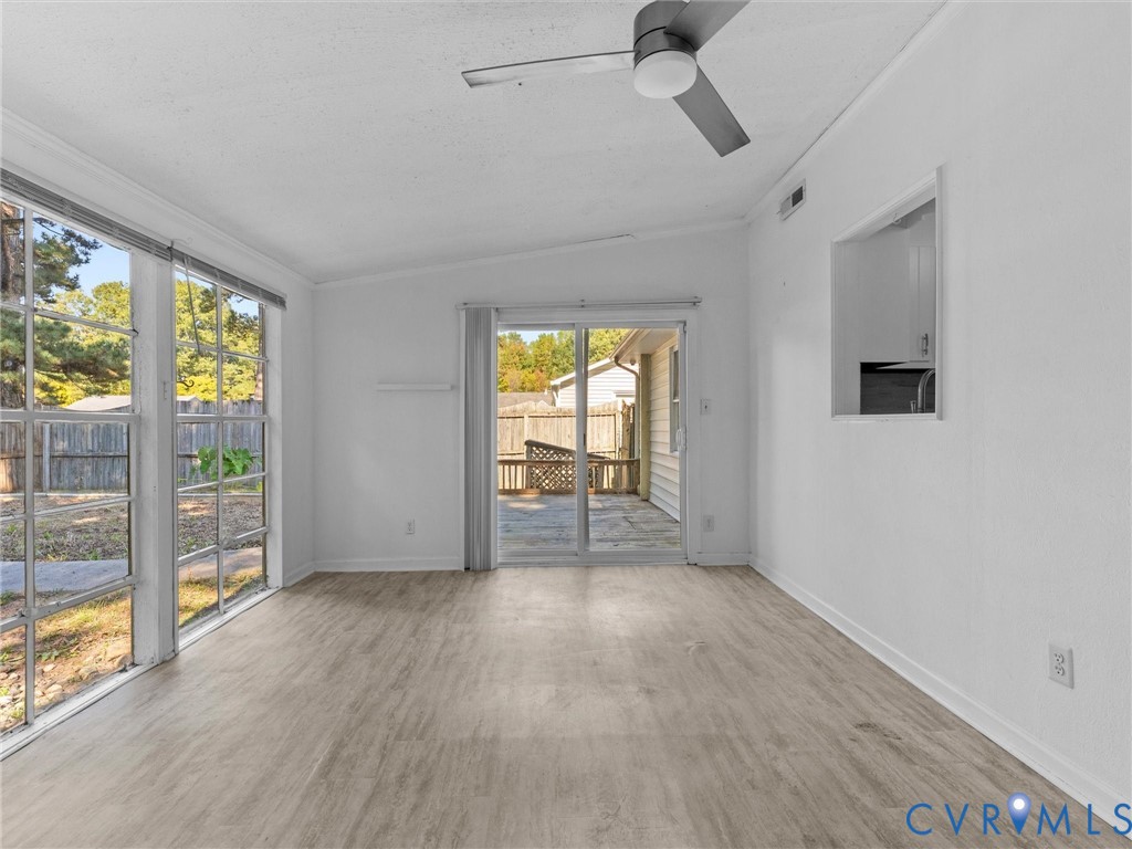 Bright room featuring wood-finish flooring, ceiling fan, large windows, and a sliding glass door providing access to the patio
