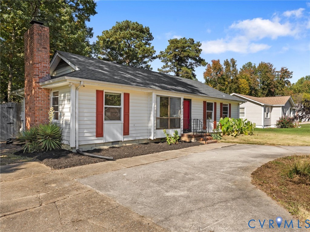 Single-story residence featuring horizontal lap siding, red window shutters, an exterior brick chimney, and a concrete driveway Single-story residence featuring horizontal lap siding, red window shutters, an exterior brick chimney, and a concrete driveway
