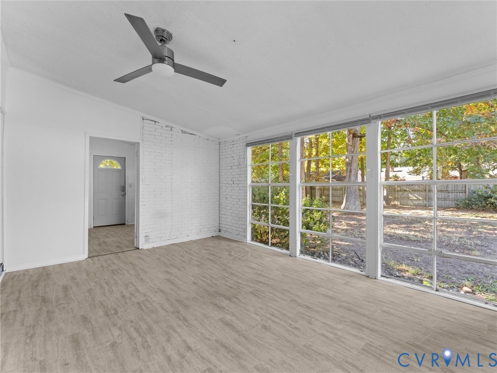 Room featuring wood-finish flooring, white painted brick walls, multi-pane windows, and a ceiling-mounted light fixture