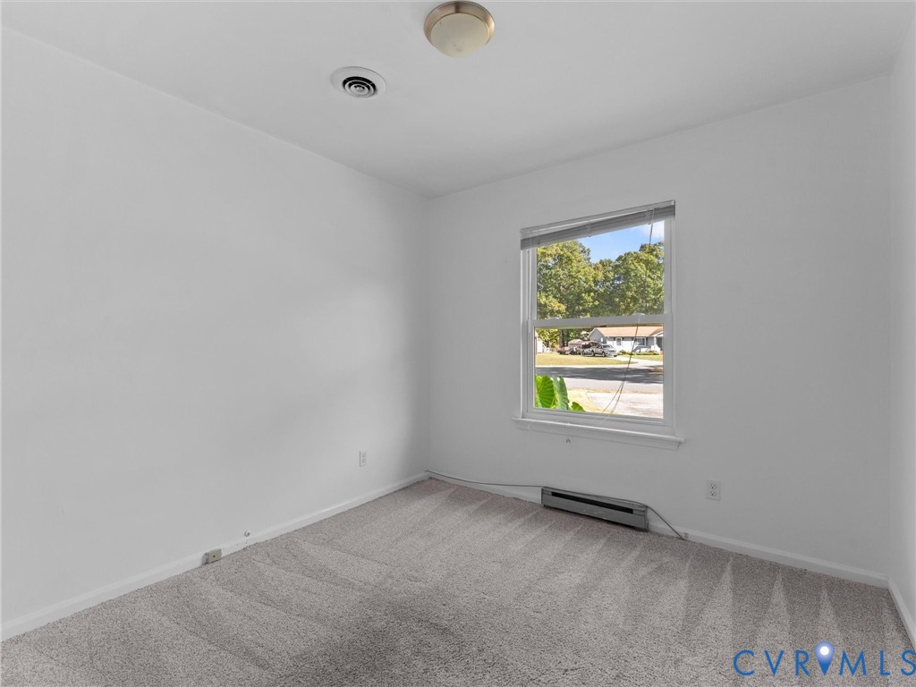 Neutral-toned carpeted flooring, single-pane window with a horizontal blind, and a flush-mount ceiling light fixture
