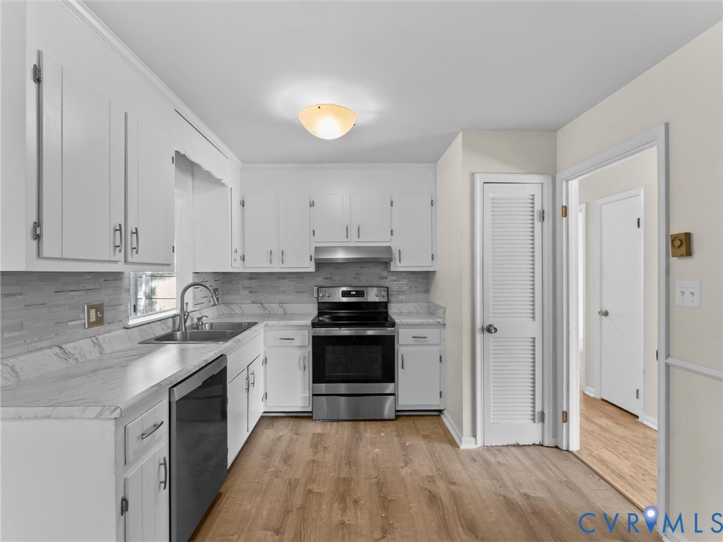 Kitchen featuring white cabinetry, stone-finish countertops, stainless steel appliances, a tile backsplash, and wood-finish flooring