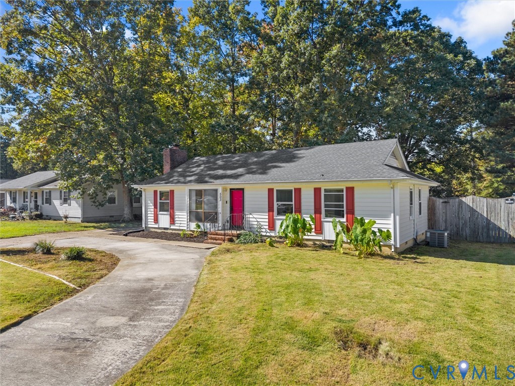 Single-story residence featuring white siding, red window shutters, an asphalt shingle roof, a brick chimney, and a concrete driveway Single-story residence featuring white siding, red window shutters, an asphalt shingle roof, a brick chimney, and a concrete driveway
