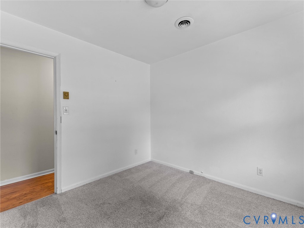 Interior room featuring neutral wall paint, wall-to-wall carpeting, and wood-finish flooring visible through the doorway