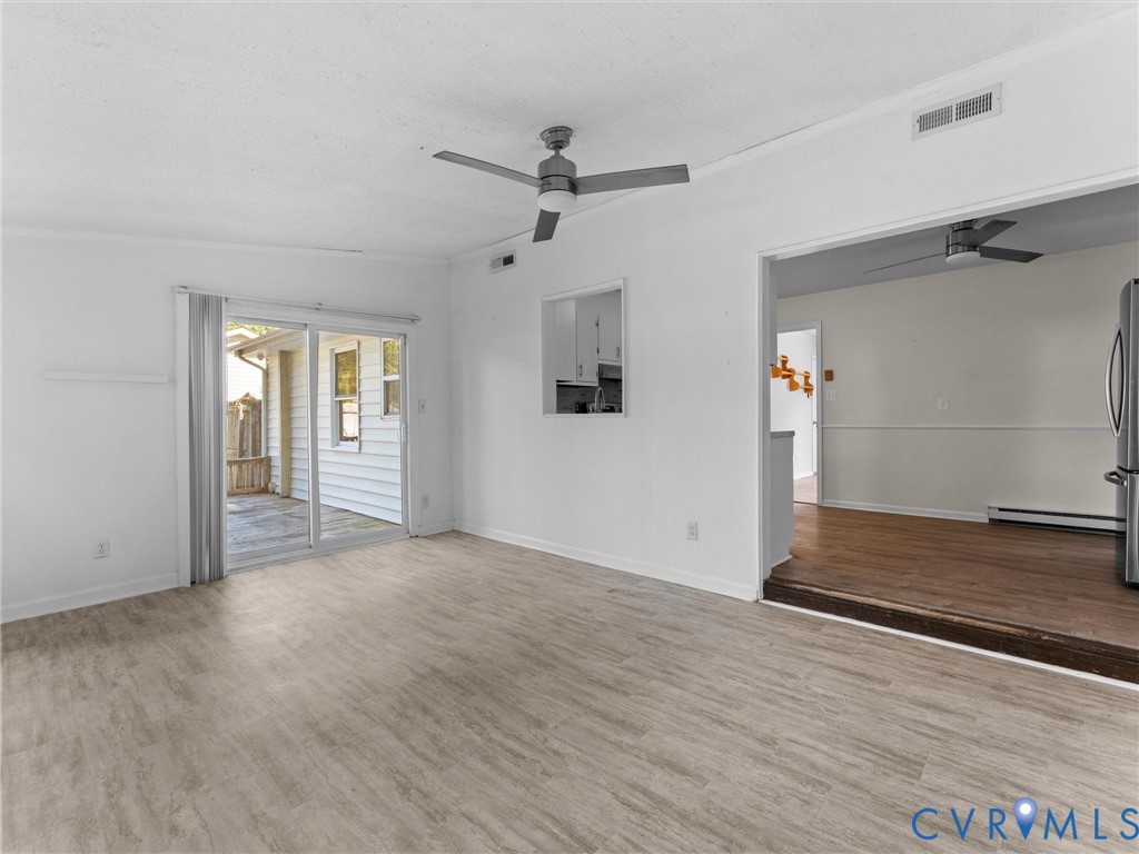 Living area featuring wood-finish flooring, a ceiling fan, and sliding glass doors providing outdoor access, with a pass-through opening to a second room finished with wood-finish flooring