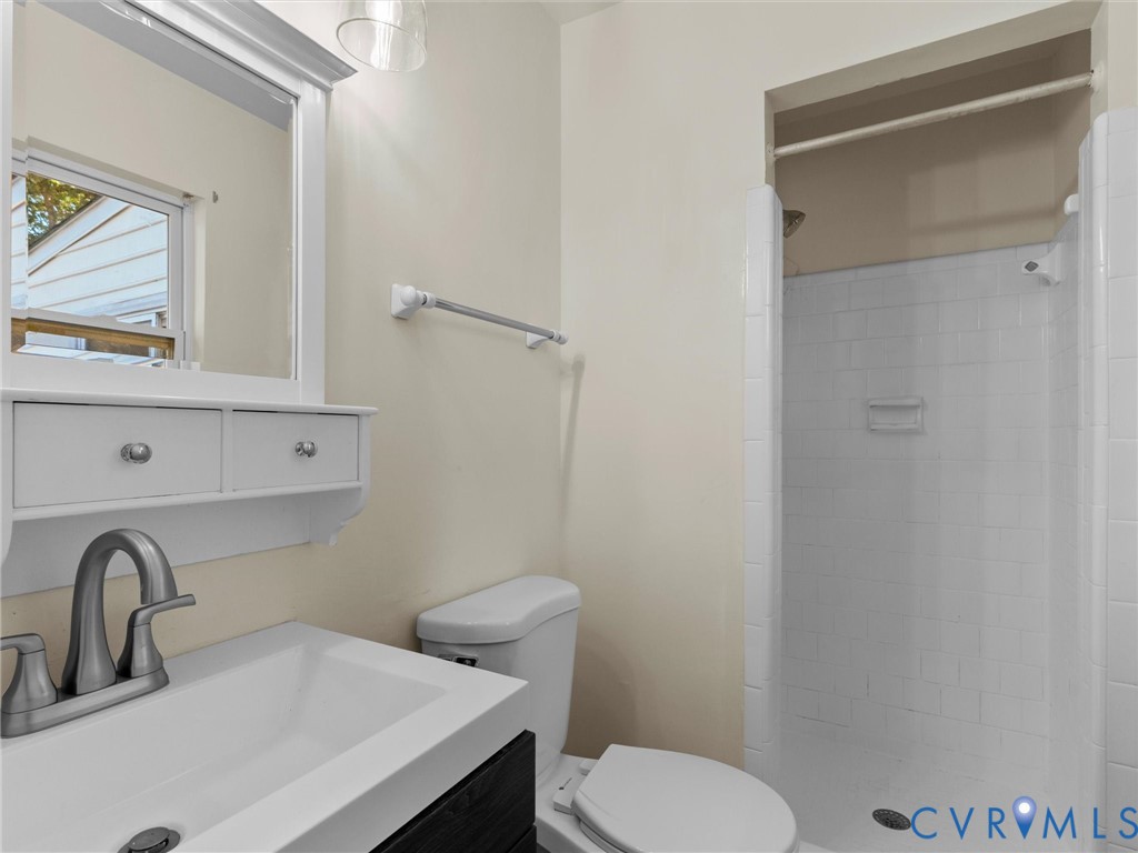 Wall-mounted vanity featuring a rectangular integrated sink, white tiled shower stall, and framed medicine cabinet