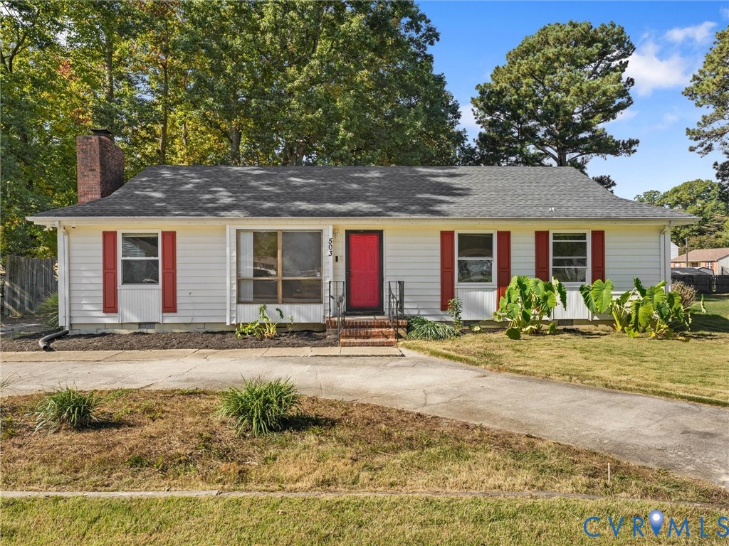 Single-story residence featuring light-colored siding, contrasting red shutters, a brick chimney, a concrete driveway, and a shingled roof Single-story residence featuring light-colored siding, contrasting red shutters, a brick chimney, a concrete driveway, and a shingled roof