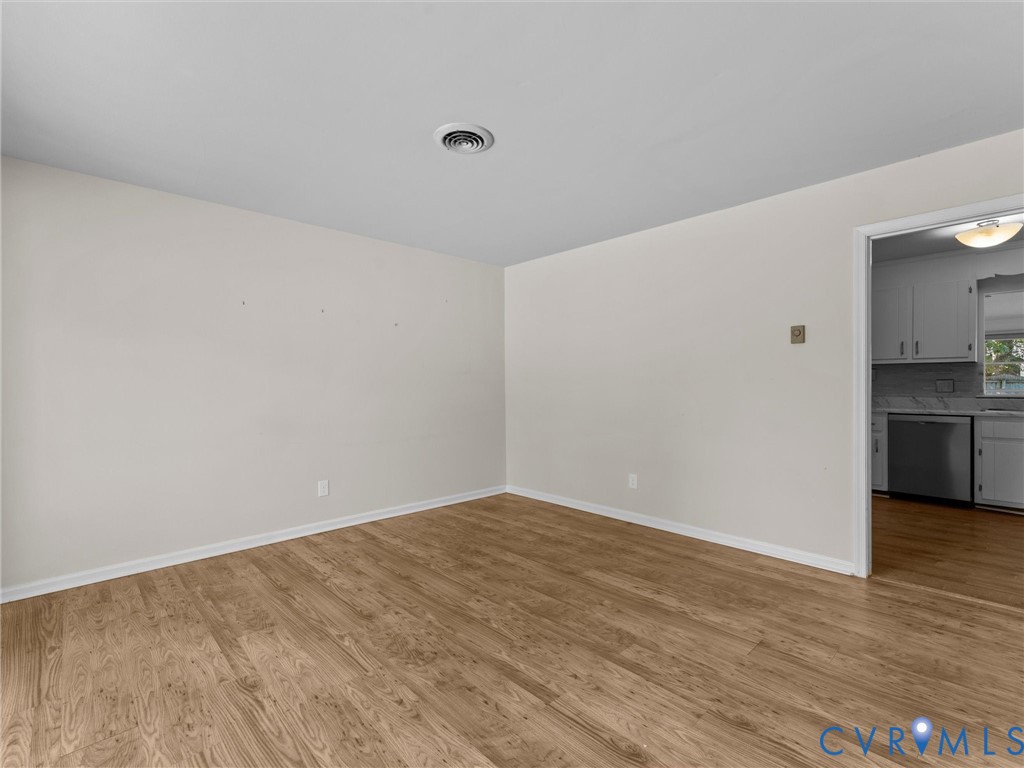 Neutral-toned interior featuring wood-finish flooring and a doorway providing a sightline to a kitchen with white cabinetry and stainless steel appliances Neutral-toned interior featuring wood-finish flooring and a doorway providing a sightline to a kitchen with white cabinetry and stainless steel appliances