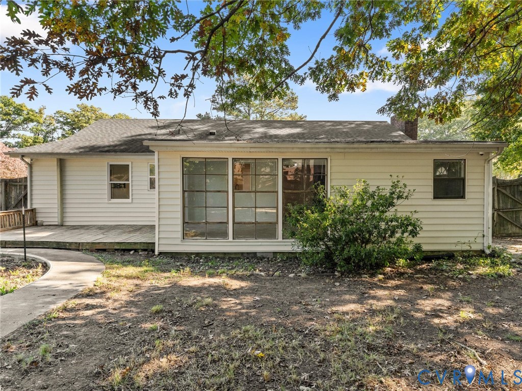 Rear exterior featuring horizontal lap siding, large paneled windows, a concrete walkway, and a wooden deck