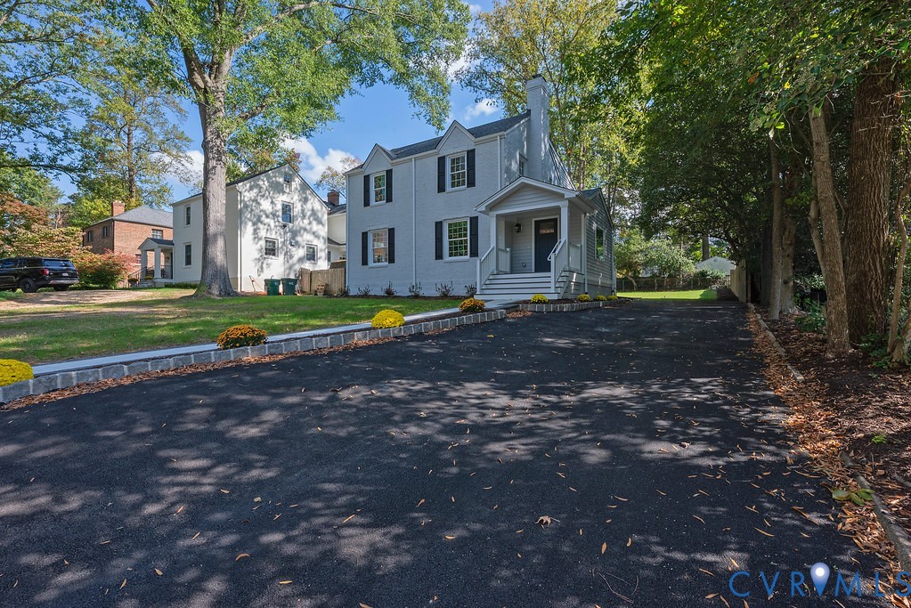 Two-story exterior featuring light-toned siding, black window shutters, a covered front entryway, and an expansive asphalt driveway Two-story exterior featuring light-toned siding, black window shutters, a covered front entryway, and an expansive asphalt driveway