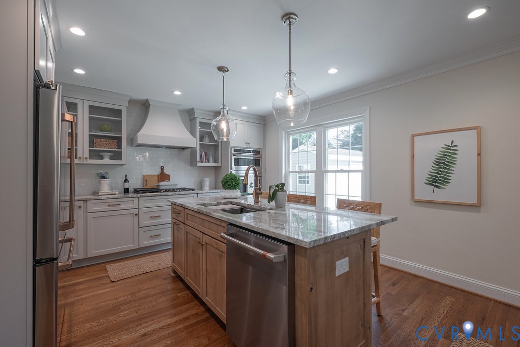 Kitchen featuring shaker-style cabinetry, natural stone countertops, a wood-finish island, stainless steel appliances, and glass pendant lighting