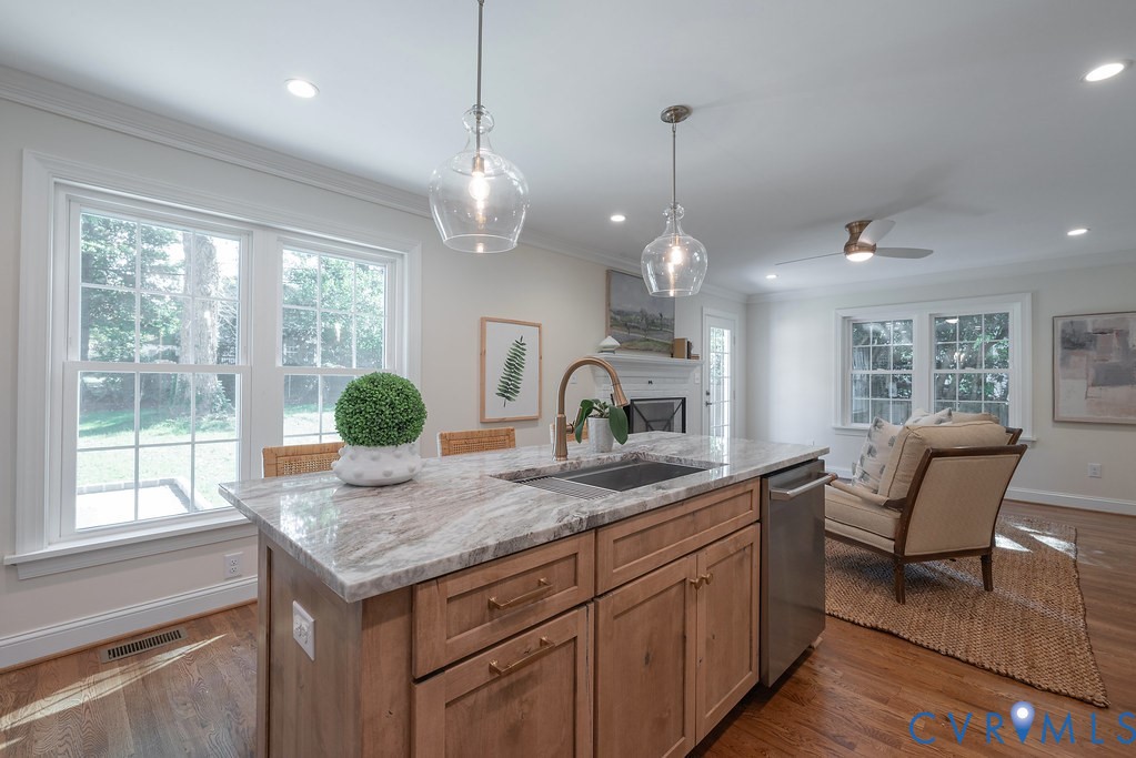 Kitchen island featuring a natural stone countertop, undermount sink with a gooseneck faucet, shaker-style wood cabinetry, and dual glass pendant lighting