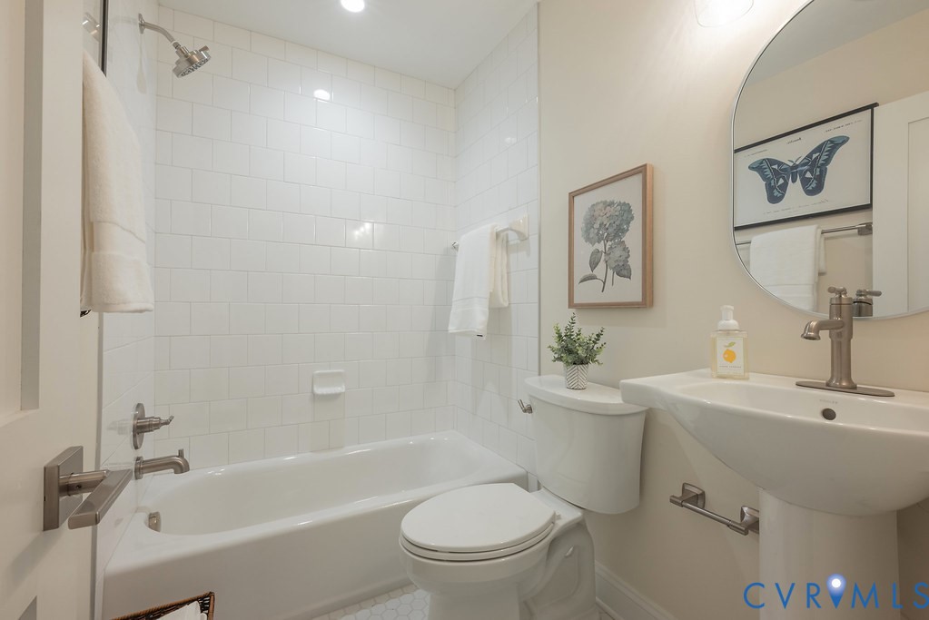 Bathroom featuring a shower-tub combination with white subway tile surround, pedestal sink with metallic faucet, and a circular wall-mounted mirror