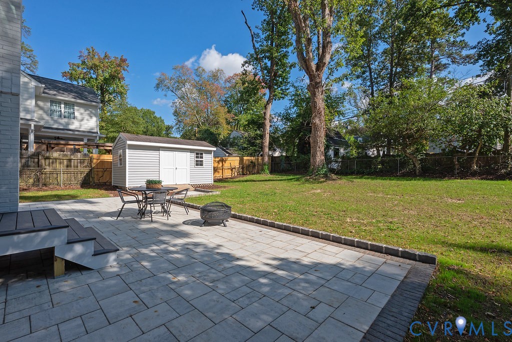 Backyard featuring a paved stone patio, a detached storage shed, a lawn, perimeter fencing, and mature trees