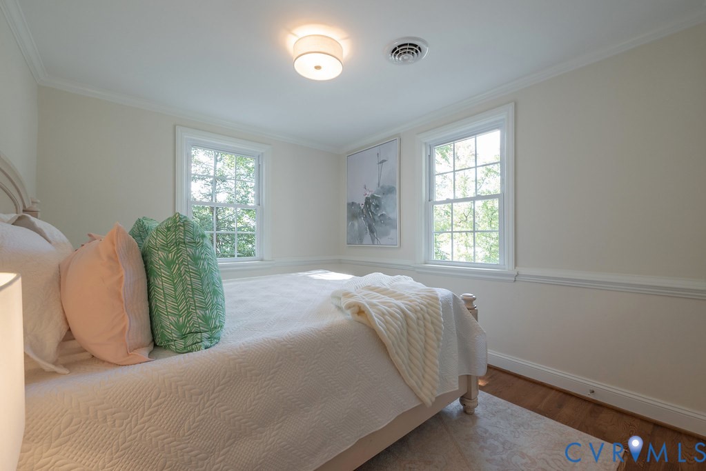Room interior featuring wood-finish flooring, white crown molding, crisp chair rail detailing, and two double-hung windows with muntins