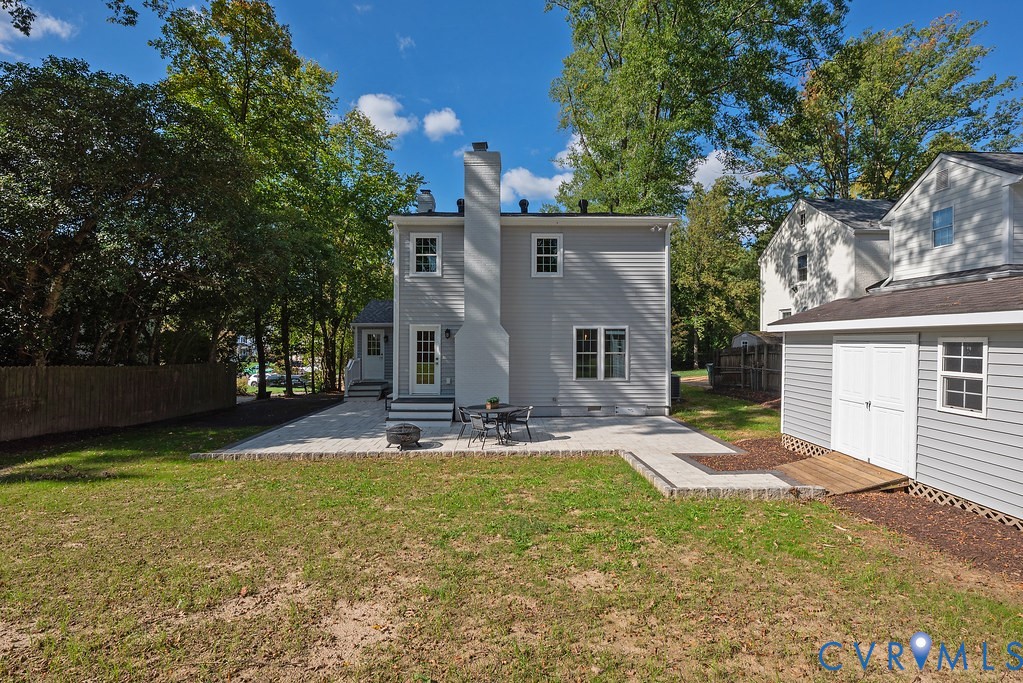 Rear exterior featuring a tall masonry chimney, light-toned paved patio, siding finish, and a detached outbuilding