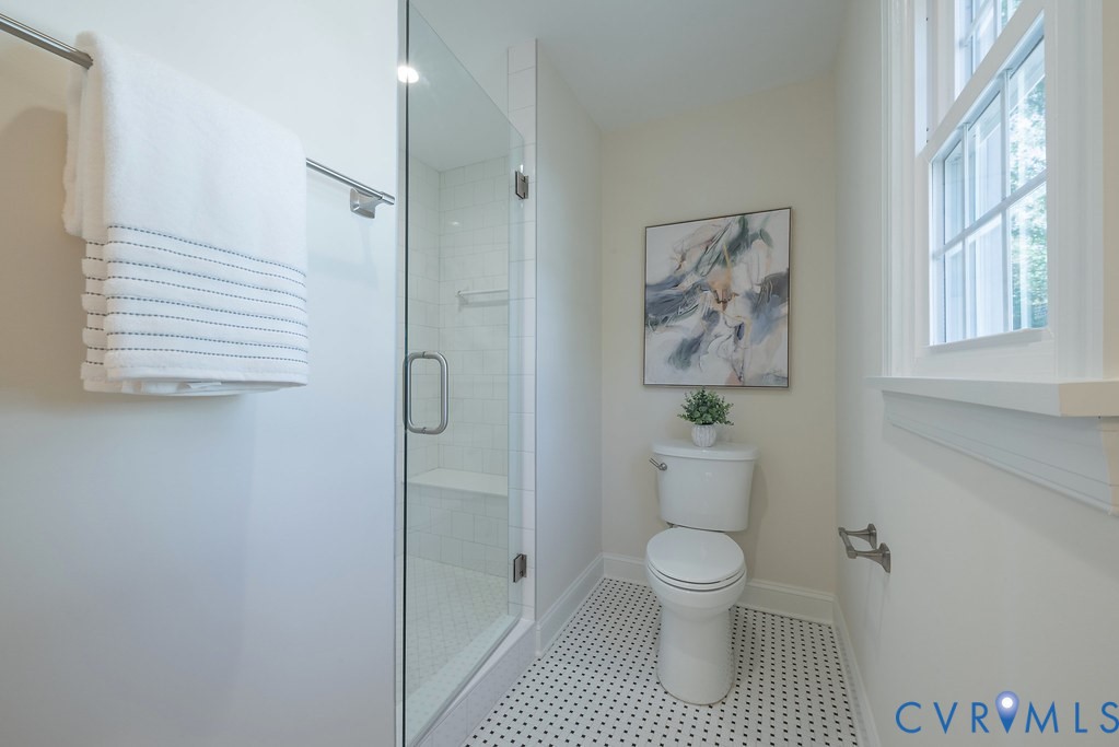 Bathroom featuring a glass-enclosed shower with tiled surround and built-in bench, geometric patterned floor tile, and double-hung window