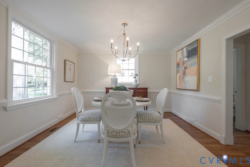 Dining area featuring wood-finish flooring, chair rail molding, crown molding, multi-pane windows, and a multi-arm metal chandelier