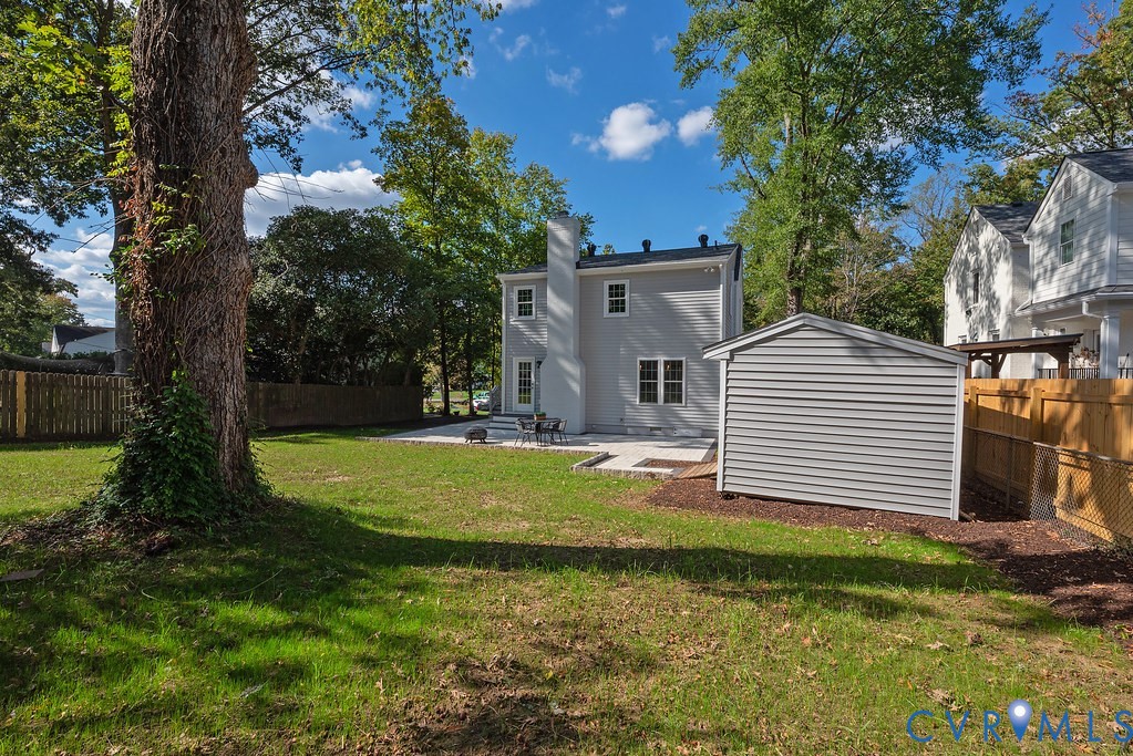 Expansive backyard featuring a manicured lawn, stone patio, detached storage structure, and perimeter privacy fencing